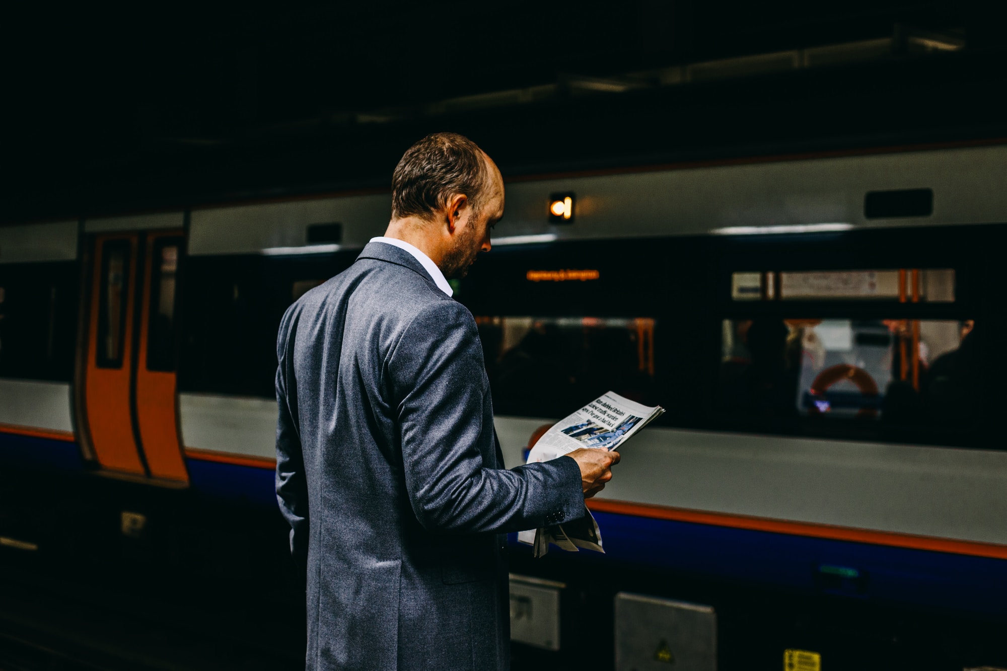 man holding newspaper standing on train station